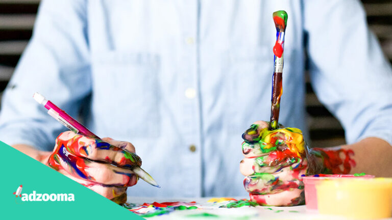 A creative man holding a pen and paintbrush covered in paint